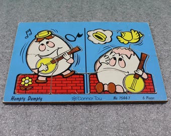 May include: A vintage wooden puzzle featuring Humpty Dumpty playing a banjo. The blue puzzle has two egg characters, musical notes, and the text "Humpty Dumpty", "Connor Toy", and "6 Pieces". The puzzle is made of six pieces.