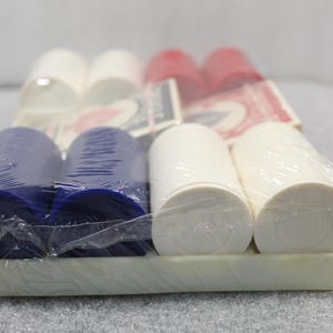 Pu&ograve; includere: Un set confezionato di fiches da poker rosse, bianche e blu. Le fiches sono cilindriche e disposte in file, con alcune carte da gioco visibili sullo sfondo. Le fiches sono avvolte in plastica trasparente.