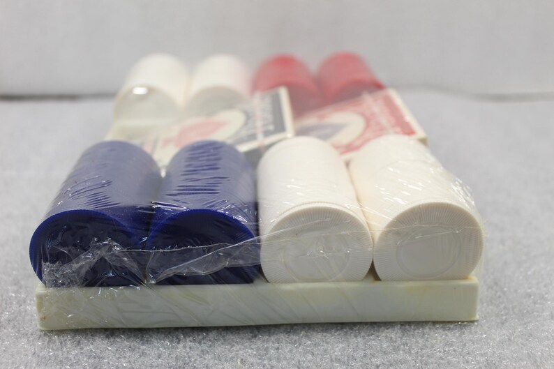 Pu&ograve; includere: Un set confezionato di fiches da poker rosse, bianche e blu. Le fiches sono cilindriche e disposte in file, con alcune carte da gioco visibili sullo sfondo. Le fiches sono avvolte in plastica trasparente.