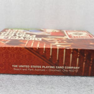 Pu&ograve; includere: Una scatola di carte da gioco Bicycle Poker. La scatola &egrave; principalmente rossa con un motivo e il testo "Bicycle Poker Size". L'indirizzo di The United States Playing Card Company &egrave; stampato sulla scatola.