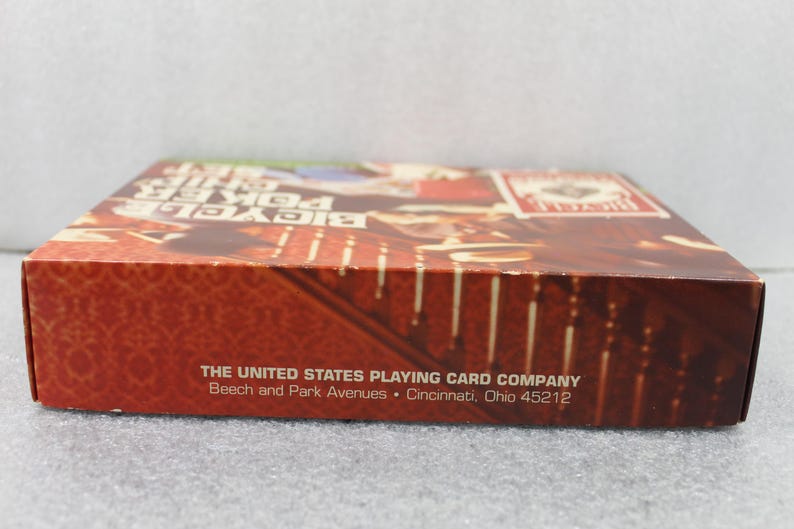 Pu&ograve; includere: Una scatola di carte da gioco Bicycle Poker. La scatola &egrave; principalmente rossa con un motivo e il testo "Bicycle Poker Size". L'indirizzo di The United States Playing Card Company &egrave; stampato sulla scatola.