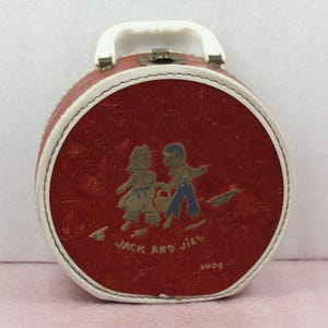 May include: A vintage, round, red case with a white handle and trim. The front features a graphic of two children with the words "Jack and Jill". The case has a metal clasp.