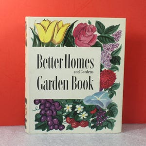 May include: A vintage "Better Homes and Gardens Garden Book" with a cream-colored cover. The cover features illustrations of yellow tulips, a pink rose, purple grapes, and other flowers. The title is in a bold, black font.