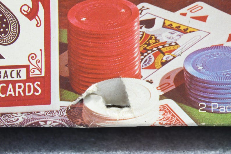 Pu&ograve; includere: Primo piano di un set da poker con fiches rosse e blu, carte da gioco e un mazzo di carte. Le carte mostrano il Re di Picche e il Dieci di Quadri. Il mazzo di carte &egrave; etichettato "BACK CARDS".