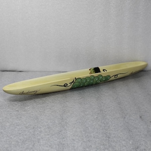 May include: A long, cream-colored wooden serving dish with the word "Chardonnay" written in black script. The dish is decorated with a green grape cluster and a black wine bottle illustration.