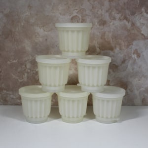 May include: Six white plastic pudding molds stacked in a pyramid shape. The molds have a fluted design and are perfect for making individual desserts.