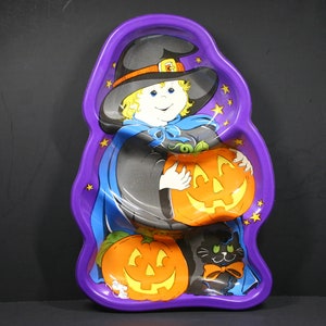 May include: A purple Halloween-themed serving tray shaped like a witch holding a jack-o'-lantern. The tray features a black cat with an orange bow tie and two carved pumpkins. The witch wears a black hat with an orange band.