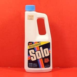 May include: A white plastic bottle of Solo heavy-duty detergent with a blue cap and handle. The label features the brand name "Solo" in large white letters, with the text "Heavy Duty Detergent Plus Fabric Softener". The bottle is 16 fl oz.