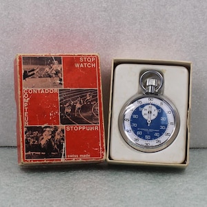 May include: A vintage stopwatch with a blue face and silver casing, displayed in its original red box. The box features illustrations of athletes and the words "STOP WATCH", "CONTADOR", and "STOPPUHR". The stopwatch is marked "swiss made".