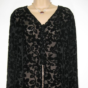 Può includere: Top nero a maniche lunghe con motivo floreale e scollo a V. Il tessuto trasparente rivela uno scorcio dell'indumento sottostante. La parte superiore ha una chiusura con bottoni sul davanti e una delicata collana.