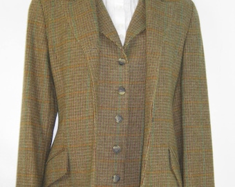May include: A brown and green tweed blazer and matching vest set featuring a subtle plaid pattern. The blazer has long sleeves and flap pockets, while the vest is buttoned down the front. A white collared shirt with a ruffled neckline is worn underneath.