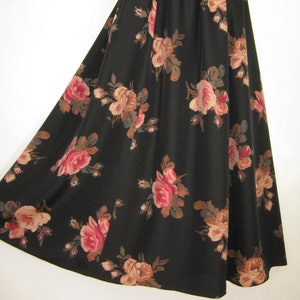 Op de afbeelding: Een lange, zwarte rok met een bloemenpatroon. De rozen zijn in tinten roze, perzik en bruin, wat een vintage esthetiek creëert. De rok heeft een geplooide taille en een volle, uitlopende silhouet.