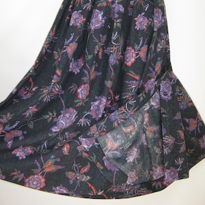 May include: A long, black skirt with a floral pattern in shades of purple, red, and green. The skirt has a high waist and a flowing silhouette, with a slit on the side. The fabric appears to be lightweight and suitable for warmer weather.