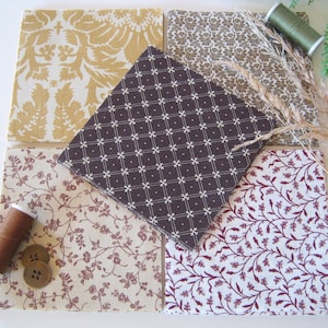 Può includere: Una collezione di campioni di tessuto in vari modelli e colori, tra cui floreali, damascati e geometrici. I campioni sono disposti con rocchetti di filo e bottoni, suggerendo un tema di cucito o artigianato. I colori includono oro, marrone e bordeaux.