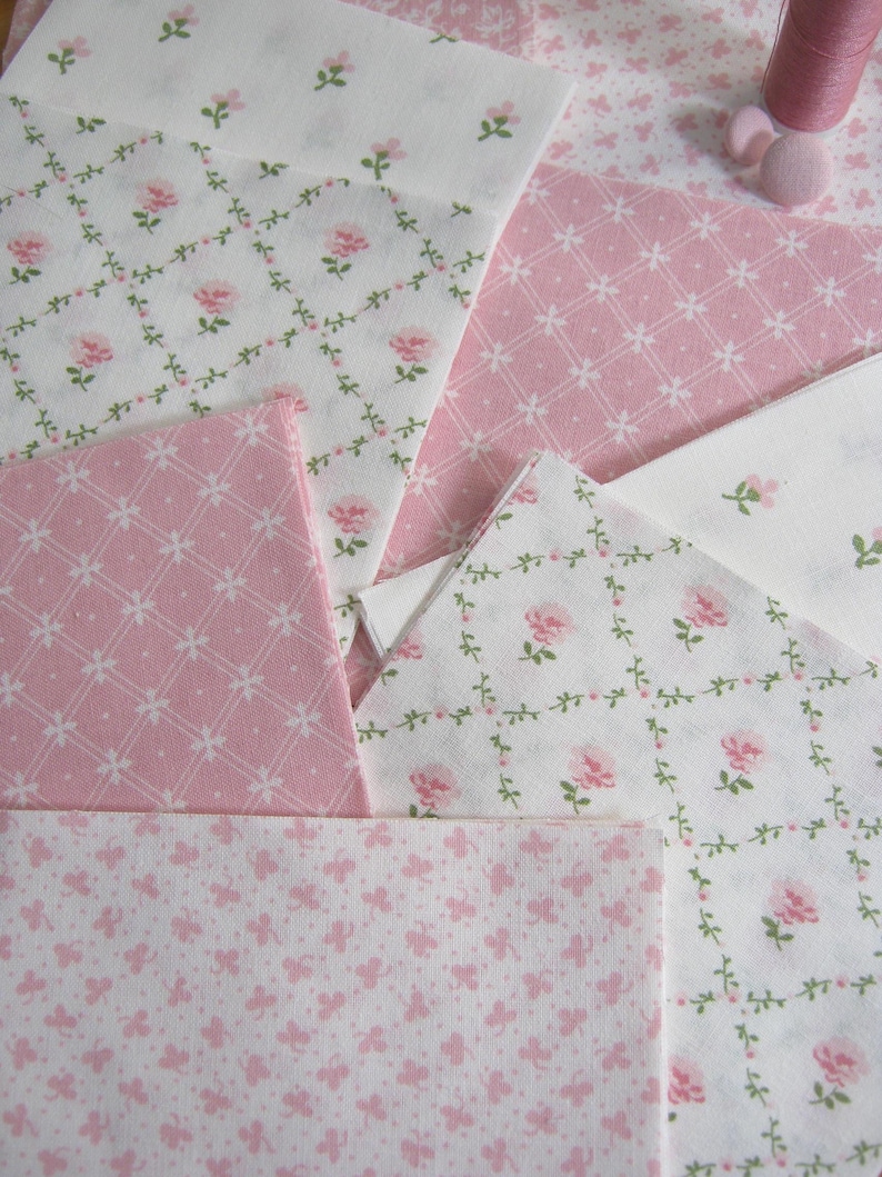Pode incluir: Variedade de quadrados de tecido floral rosa e branco. Os tecidos apresentam v&aacute;rios padr&otilde;es, incluindo rosas, vinhas e desenhos geom&eacute;tricos. Uma bobina de linha rosa e um bot&atilde;o s&atilde;o vis&iacute;veis no fundo, sugerindo um projeto de costura ou colcha.
