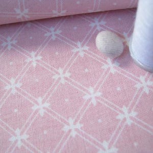 Pode incluir: Tecido rosa com um padr&atilde;o floral branco e um rolo de tecido. Uma bobina de linha branca e uma dedeira branca tamb&eacute;m est&atilde;o na imagem. O tecido tem um design em grade.