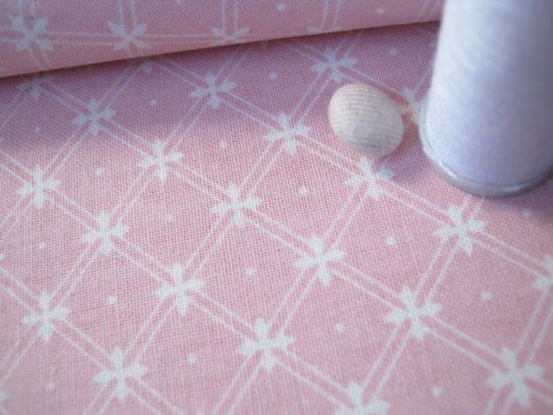 Pode incluir: Tecido rosa com um padr&atilde;o floral branco e um rolo de tecido. Uma bobina de linha branca e uma dedeira branca tamb&eacute;m est&atilde;o na imagem. O tecido tem um design em grade.