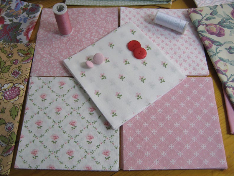 Pode incluir: Variedade de quadrados de tecido com padr&otilde;es florais e geom&eacute;tricos, em tons de rosa, branco e bege. Inclui carret&eacute;is de linha e bot&otilde;es, sugerindo um projeto de costura ou patchwork. Os tecidos est&atilde;o dispostos sobre uma superf&iacute;cie de madeira.