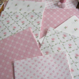 Pode incluir: Variedade de quadrados de tecido rosa e branco com estampas florais e de borboletas. Uma bobina de linha rosa e uma almofada de alfinetes rosa tamb&eacute;m s&atilde;o vis&iacute;veis. Os tecidos apresentam delicados desenhos de rosas e borboletas, perfeitos para projetos de patchwork ou artesanato.
