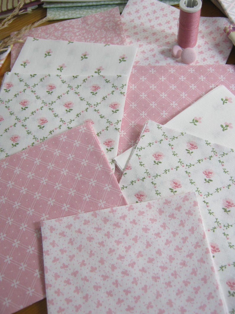 Pode incluir: Variedade de quadrados de tecido rosa e branco com estampas florais e de borboletas. Uma bobina de linha rosa e uma almofada de alfinetes rosa tamb&eacute;m s&atilde;o vis&iacute;veis. Os tecidos apresentam delicados desenhos de rosas e borboletas, perfeitos para projetos de patchwork ou artesanato.