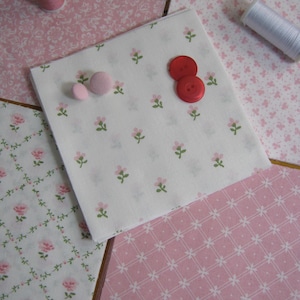 Pode incluir: Uma cole&ccedil;&atilde;o de quadrados de tecido floral rosa e branco, com carret&eacute;is de linha e bot&otilde;es vermelhos e rosa. O tecido apresenta v&aacute;rios padr&otilde;es, incluindo pequenas flores e desenhos de rosas, perfeitos para projetos de costura e artesanato.