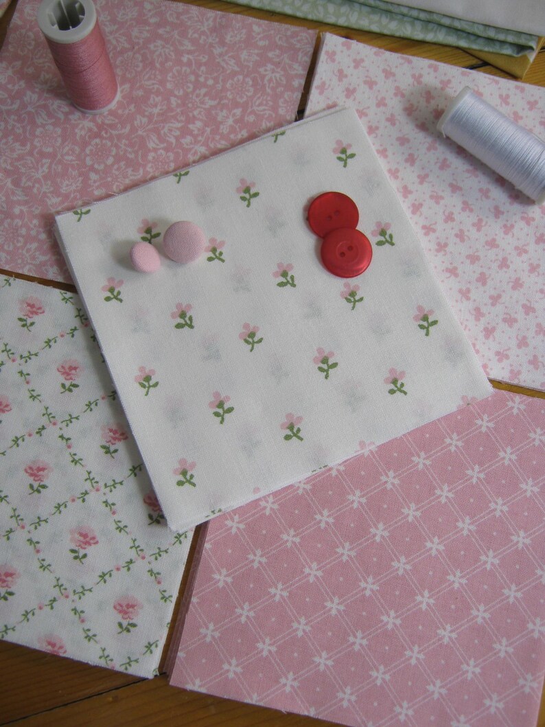 Pode incluir: Uma cole&ccedil;&atilde;o de quadrados de tecido floral rosa e branco, com carret&eacute;is de linha e bot&otilde;es vermelhos e rosa. O tecido apresenta v&aacute;rios padr&otilde;es, incluindo pequenas flores e desenhos de rosas, perfeitos para projetos de costura e artesanato.