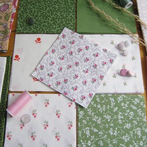 May include: A collection of fabric squares in various patterns and colors, including green, white, and floral designs. Spools of thread and small buttons are also present, suggesting a sewing or crafting theme. The fabrics feature botanical and berry motifs.