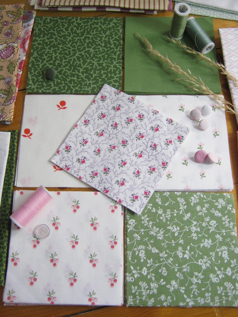 May include: A collection of fabric squares in various patterns and colors, including green, white, and floral designs. Spools of thread and small buttons are also present, suggesting a sewing or crafting theme. The fabrics feature botanical and berry motifs.
