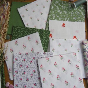 May include: Assortment of fabric squares in various floral and patterned designs. The fabrics feature white, green, and pink hues, with some displaying small floral prints and others showcasing larger botanical patterns. A spool of thread and other sewing notions are also visible.