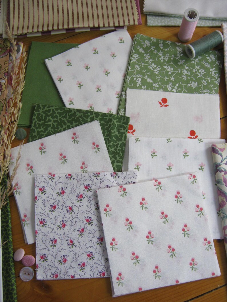 May include: Assortment of fabric squares in various floral and patterned designs. The fabrics feature white, green, and pink hues, with some displaying small floral prints and others showcasing larger botanical patterns. A spool of thread and other sewing notions are also visible.