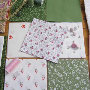 May include: Assortment of fabric squares in various patterns and colors, including floral, berry, and solid green. Spools of thread and small buttons are also present, suggesting a sewing or quilting project.