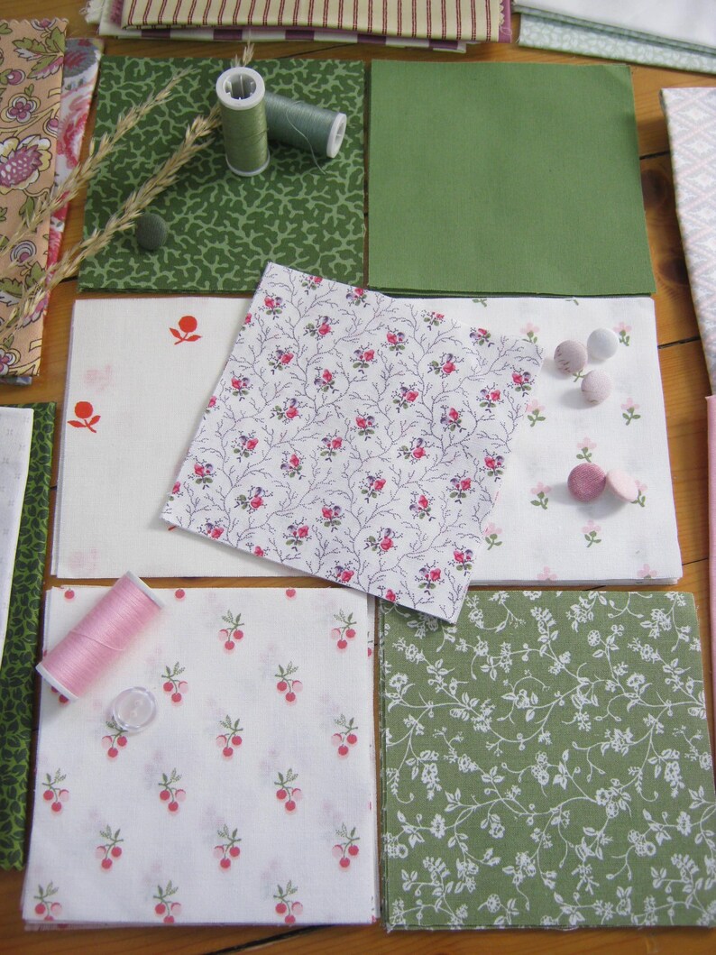 May include: Assortment of fabric squares in various patterns and colors, including floral, berry, and solid green. Spools of thread and small buttons are also present, suggesting a sewing or quilting project.