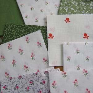 May include: Assortment of fabric swatches in various floral patterns. Includes white fabric with small pink flowers, green fabric with white floral designs, and solid green fabric. The fabrics are suitable for quilting or crafting projects.