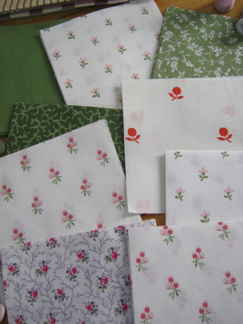 May include: Assortment of fabric swatches in various floral patterns. Includes white fabric with small pink flowers, green fabric with white floral designs, and solid green fabric. The fabrics are suitable for quilting or crafting projects.