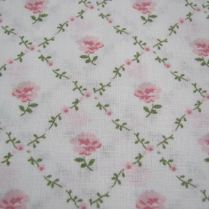 Pode incluir: Tecido branco com um padr&atilde;o repetido de rosas cor-de-rosa e folhas verdes, dispostas em uma grade de losangos. As rosas est&atilde;o em plena flora&ccedil;&atilde;o e as folhas s&atilde;o pequenas e delicadas. O design geral &eacute; suave e feminino.