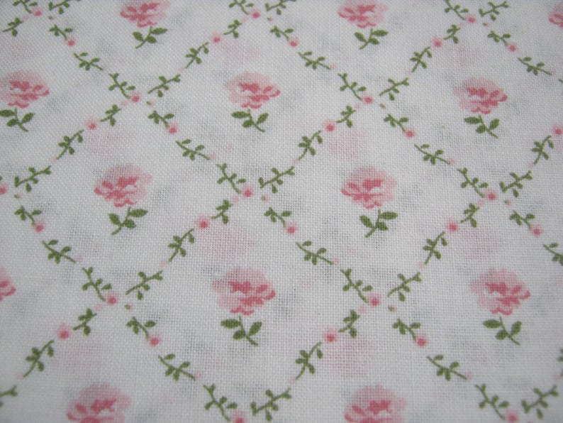 Pode incluir: Tecido branco com um padr&atilde;o repetido de rosas cor-de-rosa e folhas verdes, dispostas em uma grade de losangos. As rosas est&atilde;o em plena flora&ccedil;&atilde;o e as folhas s&atilde;o pequenas e delicadas. O design geral &eacute; suave e feminino.