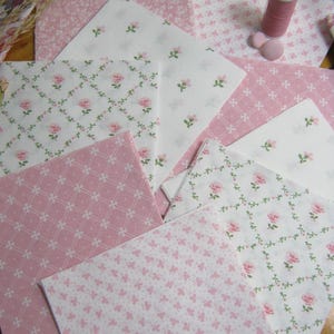 Pode incluir: Variedade de quadrados de tecido rosa e branco com desenhos florais e estampados. Uma bobina de linha rosa e dois bot&otilde;es rosa tamb&eacute;m s&atilde;o vis&iacute;veis. Ideal para projetos de quilting ou artesanato.