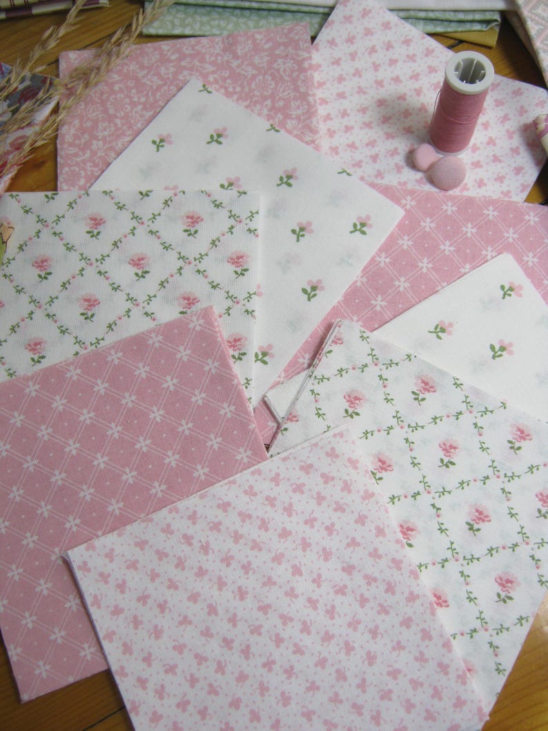 Pode incluir: Variedade de quadrados de tecido rosa e branco com desenhos florais e estampados. Uma bobina de linha rosa e dois bot&otilde;es rosa tamb&eacute;m s&atilde;o vis&iacute;veis. Ideal para projetos de quilting ou artesanato.
