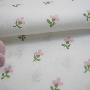 Pode incluir: Tecido branco com um padr&atilde;o repetido de pequenas flores rosa e caules verdes. Dois bot&otilde;es rosa revestidos de tecido s&atilde;o vis&iacute;veis. O tecido tem uma apar&ecirc;ncia ligeiramente texturizada, sugerindo uma fibra natural como algod&atilde;o ou linho.