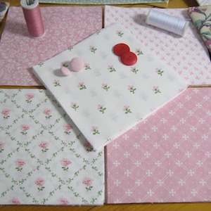 Pode incluir: Uma cole&ccedil;&atilde;o de quadrados de tecido em v&aacute;rios designs florais e estampados, incluindo tecidos rosa e brancos com pequenas flores rosa e vinhas verdes. Dois carret&eacute;is de linha e v&aacute;rios bot&otilde;es tamb&eacute;m s&atilde;o vis&iacute;veis, sugerindo um projeto de costura ou colcha.