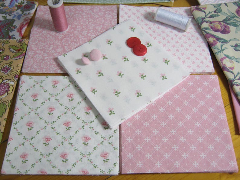 Pode incluir: Uma cole&ccedil;&atilde;o de quadrados de tecido em v&aacute;rios designs florais e estampados, incluindo tecidos rosa e brancos com pequenas flores rosa e vinhas verdes. Dois carret&eacute;is de linha e v&aacute;rios bot&otilde;es tamb&eacute;m s&atilde;o vis&iacute;veis, sugerindo um projeto de costura ou colcha.