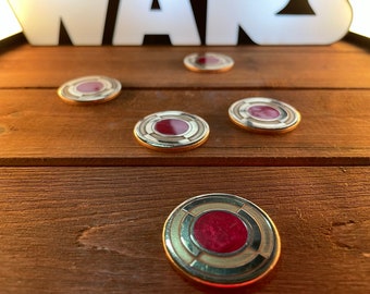 May include: Five gold-colored circular tokens with a red center and white concentric circles. The tokens are on a wooden surface.