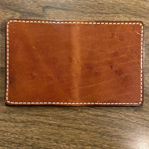 May include: A brown leather wallet with white stitching around the edges.