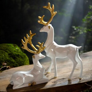 May include: Two white deer figurines with gold antlers are displayed on a wooden surface. One deer is standing, and the other is lying down. The background is a blurred forest scene with sunlight.