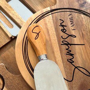 K&ouml;nnte beinhalten: K&auml;sebrett-Set aus Holz mit rundem Schneidebrett, K&auml;semesser und Servierutensilien. Das Brett ist mit dem Namen "Sampson Family" graviert. Das K&auml;semesser hat einen Holzgriff und eine Edelstahlklinge.