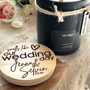 May include: A black soy wax candle with a gold lid and a wooden wick. The candle is labeled "4405 WEST" and "ocean rose". The candle is packaged with a wooden lid that says "smells like our wedding day Jenna & Selvin 5.5.24".