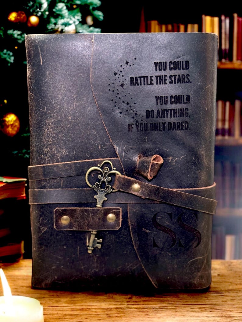 May include: A dark brown leather journal with a strap closure and a decorative key. The journal has the text "YOU COULD RATTLE THE STARS. YOU COULD DO ANYTHING, IF YOU ONLY DARED." embossed on the cover. The initials "SS" are also visible.