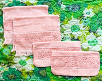 May include: Four peach-colored, vintage terry cloth towels with decorative floral embroidery. The towels are arranged on a green and white floral patterned quilt. The towels have a fringed edge.