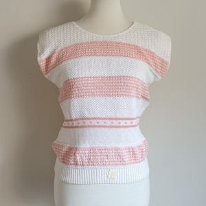 May include: A white and peach striped knitted top. The short-sleeved top has horizontal stripes in peach and white, with a textured knit pattern. The bottom hem and neckline are ribbed. A small tag is visible near the bottom hem.