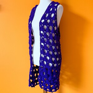 May include: A purple crochet vest with a lacy openwork design. The vest is sleeveless and has a deep V-neck.